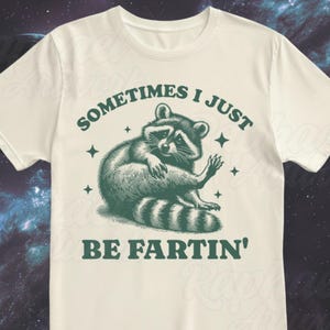 Pode incluir: Uma camiseta branca com um gr&aacute;fico de guaxinim verde e o texto "Sometimes I just be fartin'" impresso nela.