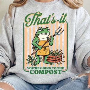 May include: A light gray sweatshirt with a graphic of a frog holding a pitchfork, wearing an apron, and standing next to a compost bin. The text reads "That's-it, You're going to the Compost."