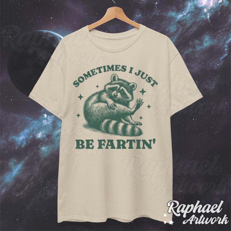 Pode incluir: Uma camiseta bege com um gr&aacute;fico de guaxinim verde e o texto "Sometimes I just be fartin'" impresso na frente.