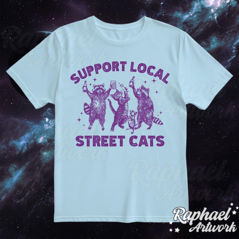 May include: Light blue t-shirt with a purple graphic of raccoons holding drinks and the text "Support Local Street Cats".