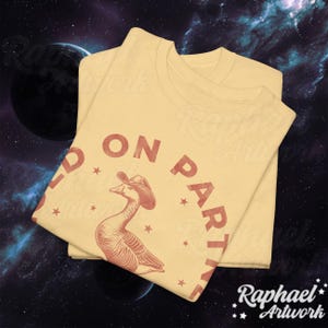 May include: A yellow t-shirt with a red graphic of a goose wearing a cowboy hat. The text "Hold On Partner" is printed around the goose in a red circular design.