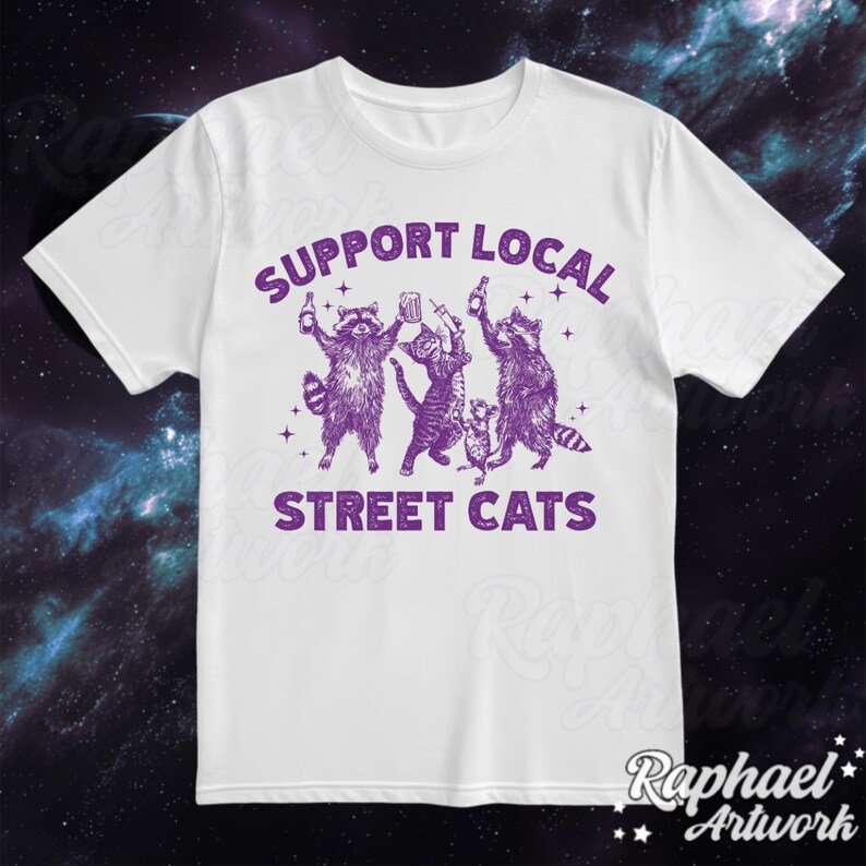 May include: White t-shirt with a purple graphic of raccoons holding drinks and the text "Support Local Street Cats".