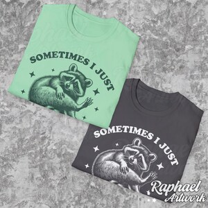 Pode incluir: Duas camisetas com um gr&aacute;fico de guaxinim e o texto "Sometimes I just" impresso nelas. As camisetas s&atilde;o verde e cinza.