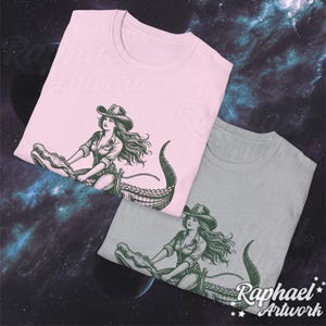 K&ouml;nnte beinhalten: Zwei T-Shirts mit einem grafischen Aufdruck einer Frau im Cowboyhut, die auf einem Alligator reitet. Die T-Shirts sind rosa und grau.