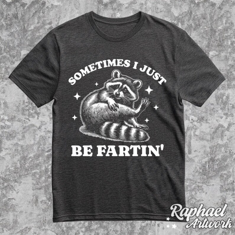Pode incluir: Uma camiseta cinza escura com um gr&aacute;fico branco de um guaxinim e o texto "Sometimes I Just Be Fartin'" impresso na frente.