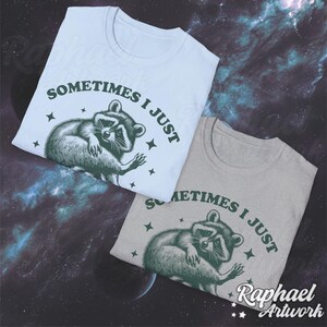 Pode incluir: Duas camisetas com um gr&aacute;fico de guaxinim e o texto "Sometimes I just" em letras verdes. As camisetas s&atilde;o azul claro e cinza.