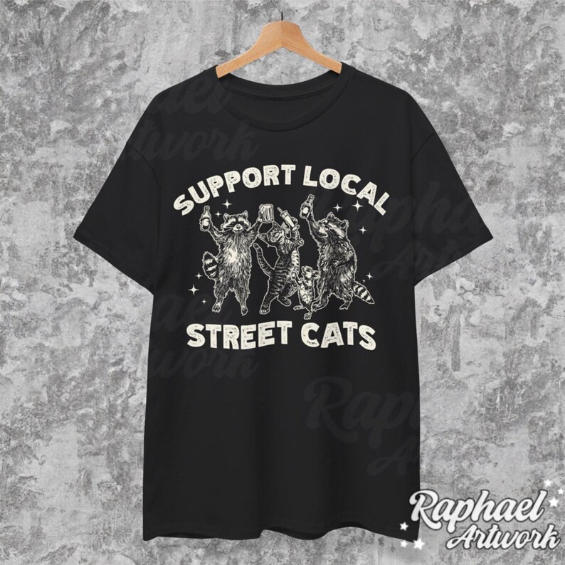 May include: Black t-shirt with a white graphic of raccoons drinking beer and the text "Support Local Street Cats".