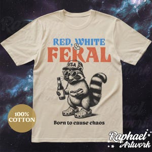 Peut inclure: Un t-shirt beige avec un graphique d'un raton laveur portant un chapeau "USA", des lunettes de soleil et tenant une bi&egrave;re et un hot-dog. Le texte "RED, WHITE & FERAL" est au-dessus du raton laveur et "Born to cause chaos" est en dessous du raton laveur.