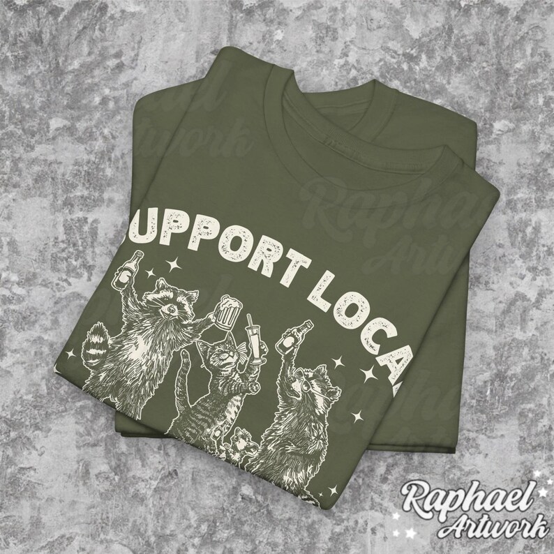 May include: A green t-shirt with the text "Support Local" printed in white. The shirt features a graphic of four raccoons drinking and holding drinks.