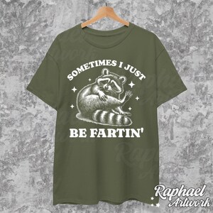 Pode incluir: Uma camiseta verde com um gr&aacute;fico branco de um guaxinim com o texto "Sometimes I Just Be Fartin'"