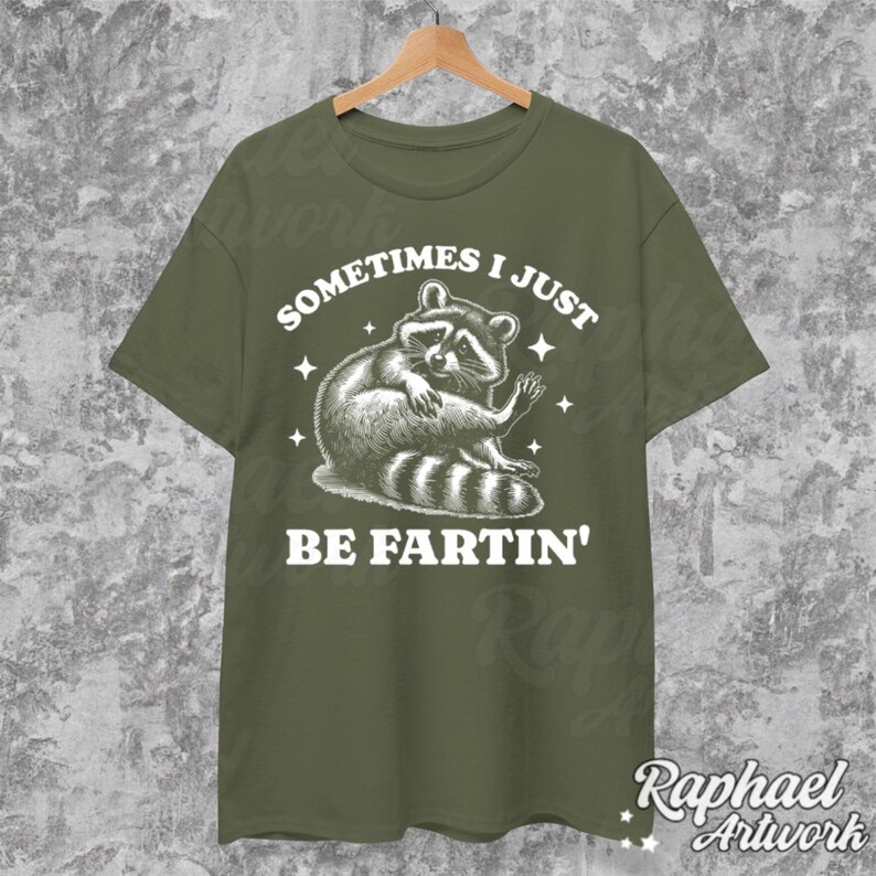 Pode incluir: Uma camiseta verde com um gr&aacute;fico branco de um guaxinim com o texto "Sometimes I Just Be Fartin'"
