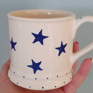 Puede incluir: Taza de cer&aacute;mica blanca con un patr&oacute;n de estrellas azules y lunares blancos alrededor de la base.