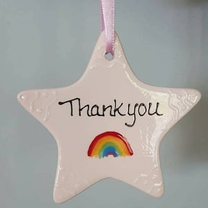 May include: White ceramic star-shaped ornament with a rainbow and the words "Thank you" written in black.