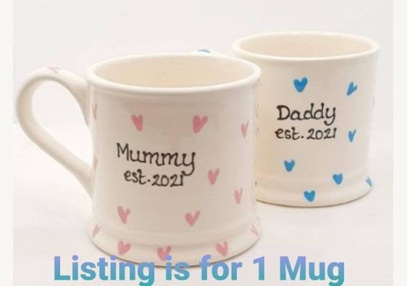 Puede incluir: Dos tazas de cer&aacute;mica blanca con corazones rosas y azules. Una taza dice "Mummy est. 2021" y la otra dice "Daddy est. 2021".