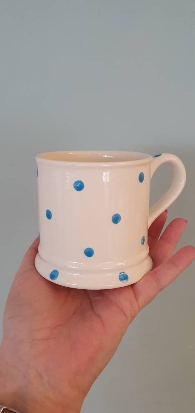 Puede incluir: Una taza de cer&aacute;mica blanca con un patr&oacute;n de lunares azules. La taza tiene un asa y una base redondeada.