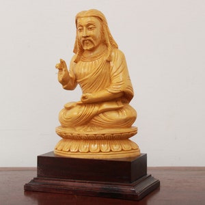 May include: A wooden statue of a person sitting in a meditative pose with their hands in their lap. The statue is painted a light yellow color and is sitting on a wooden base.