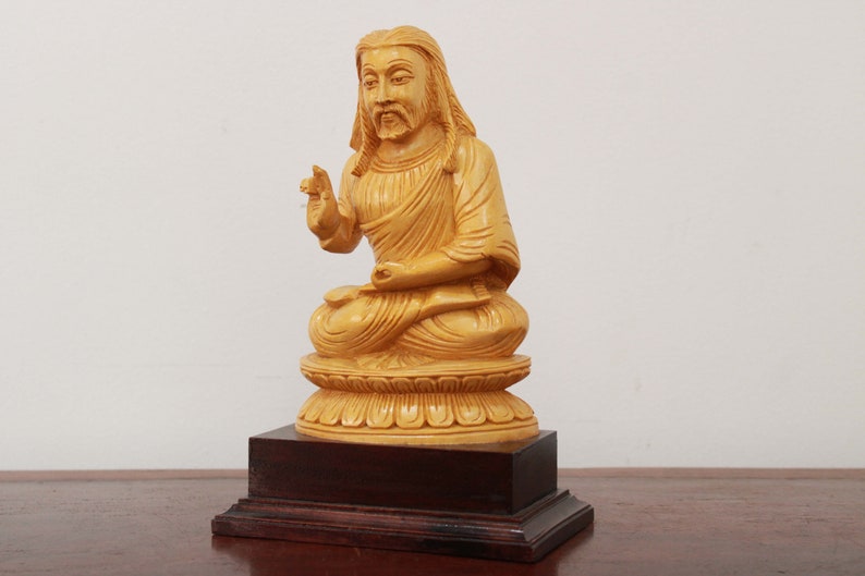 May include: A wooden statue of a person sitting in a meditative pose with their hands in their lap. The statue is painted a light yellow color and is sitting on a wooden base.