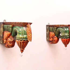 Puede incluir: Dos piezas de decoración de pared de madera talladas a mano. Cada pieza presenta un diseño detallado con colores naranja, verde y marrón. Las piezas tienen una forma única con un elemento decorativo inferior y un pequeño gancho de metal para colgar.