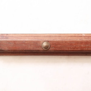 Puede incluir: Un perchero de pared de madera con tres ganchos de latón. El perchero es de color marrón oscuro y tiene una forma rectangular.