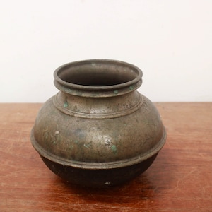 Può includere: Un piccolo vaso di ottone antico rotondo con una patina usurata e invecchiata. Il vaso ha un'ampia apertura e un fondo leggermente arrotondato.