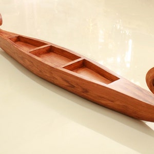 May include: A wooden boat-shaped serving tray with three compartments. The tray is made of dark brown wood and has a carved, spiral design at each end.