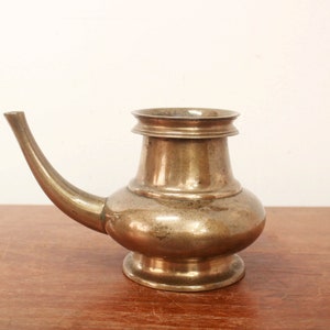 May include: A small, antique brass teapot with a curved spout. The teapot has a rounded body and a simple, elegant design.