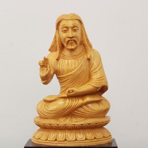 May include: A wooden statue of a person sitting in a meditative pose with their hands in their lap. The statue is carved from light brown wood and has a detailed face and clothing.