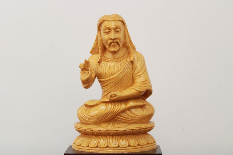 May include: A wooden statue of a person sitting in a meditative pose with their hands in their lap. The statue is carved from light brown wood and has a detailed face and clothing.