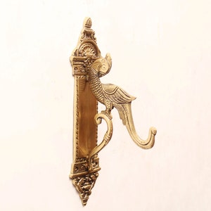 May include: Ornate brass wall hook featuring a bird design. The hook is mounted on a rectangular backplate with detailed carvings. The bird has a curved beak and detailed feathering. The hook extends downward, creating a functional and decorative piece.