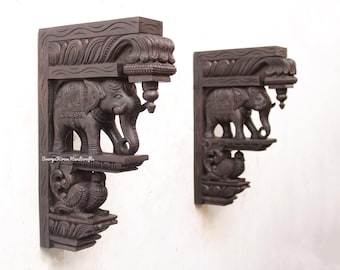 May include: Two intricately carved wooden wall brackets featuring elephants and peacocks. The brackets are dark brown and have a traditional Indian design.