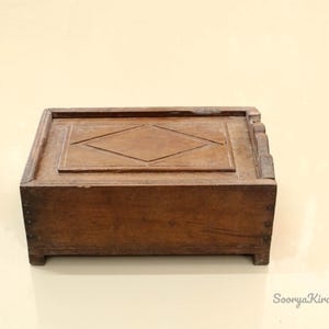 May include: A wooden box with a diamond-shaped design on the top. The box is brown and has a simple, rustic look.