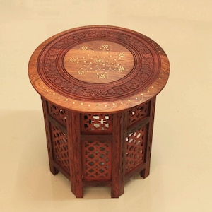 Puede incluir: Una mesa auxiliar de madera hecha a mano con una parte superior redonda y intrincados patrones florales tallados. La mesa tiene un acabado marrón oscuro y lados calados, de aproximadamente 51 cm de altura.