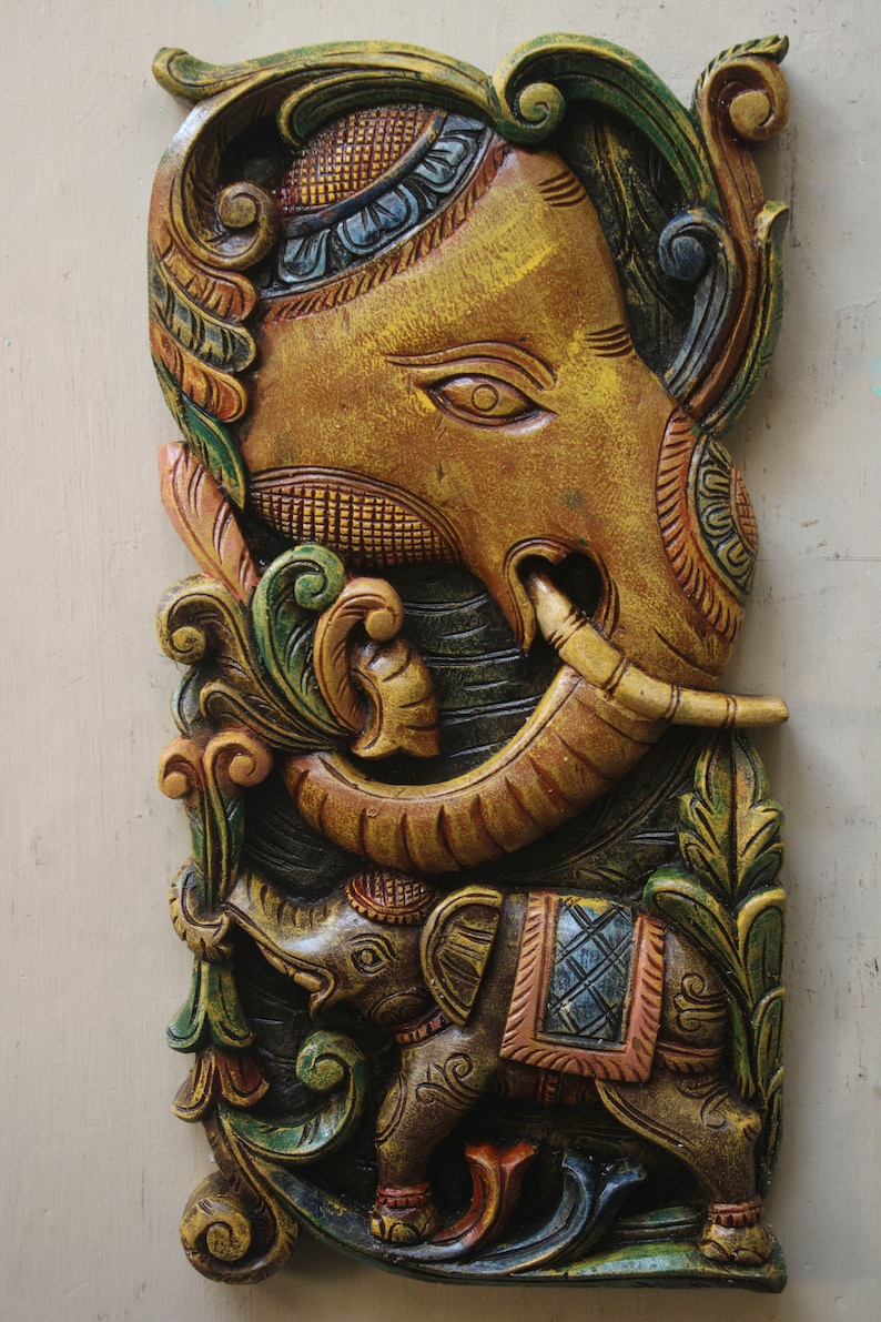 May include: A carved wooden wall hanging featuring a large, intricately detailed elephant with a smaller elephant at its feet. The elephants are painted in shades of brown, green, and blue, with intricate floral designs.