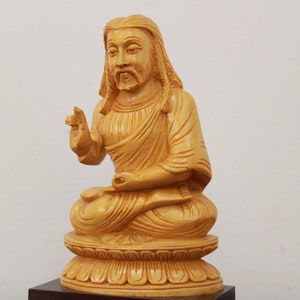 May include: A wooden statue of a person sitting in a meditative pose with their hands in their lap. The statue is carved from light brown wood and has a detailed face with a long beard.