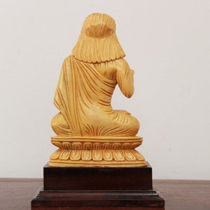 May include: A wooden statue of a person sitting in a meditative pose. The statue is painted in a light yellow color and is on a wooden base.