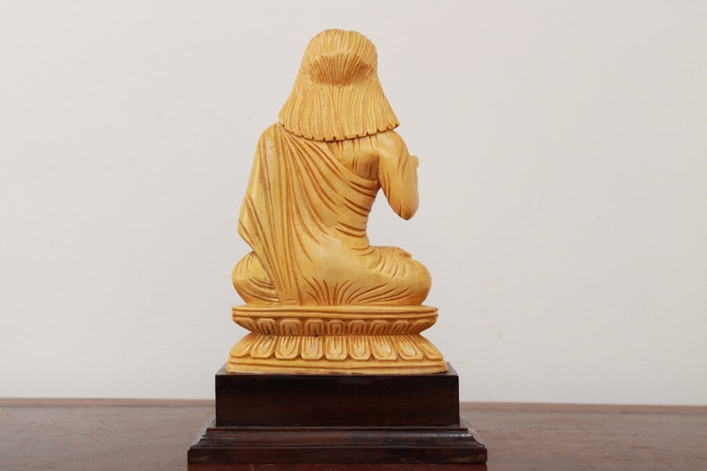May include: A wooden statue of a person sitting in a meditative pose. The statue is painted in a light yellow color and is on a wooden base.