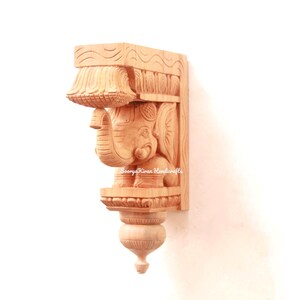 May include: A wooden wall bracket with an intricately carved elephant design. The bracket is made of light brown wood and has a decorative, ornate design.