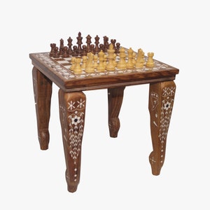 May include: A wooden chessboard table with intricate ivory inlay designs on the legs. The table has a traditional chessboard design with a light brown and white checkered pattern. The chess pieces are arranged on the board in a game in progress.
