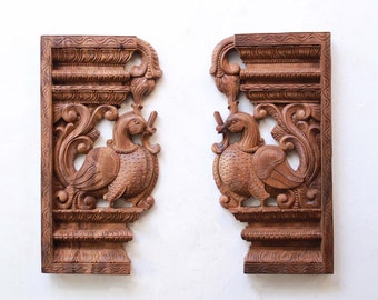 May include: Two intricately carved wooden wall decor pieces featuring peacocks with elaborate tail feathers and floral designs. The pieces are made of dark brown wood and have a traditional Indian style.