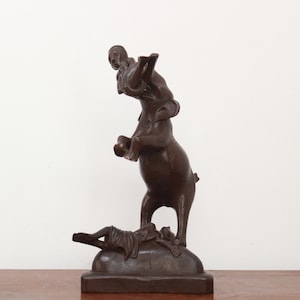 Può includere: Una scultura in legno marrone scuro di una persona che cavalca un elefante. L'elefante è in piedi sulle zampe posteriori e la persona si tiene aggrappata alla sua schiena. La scultura è su una base in legno.