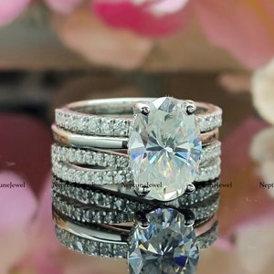 May include: A silver ring set with a large oval-shaped diamond, surrounded by smaller diamonds. The ring is set on a white background with pink flowers.