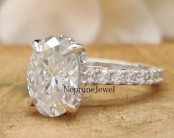 May include: A silver engagement ring with an oval-shaped center stone and a pave diamond band. The ring is set on a wooden surface.