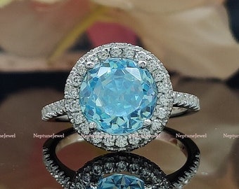 May include: A silver ring with a large, oval-shaped, light blue gemstone surrounded by a halo of smaller, clear gemstones.