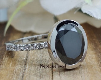May include: A silver ring with a black oval gemstone set in a bezel setting. The ring has a band of small diamonds.