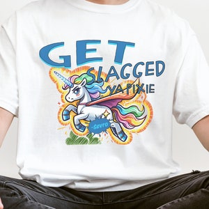 Puede incluir: Camiseta blanca con un gráfico de unicornio azul, amarillo y arcoíris y el texto "GET SLAGGED YA PIXIE".