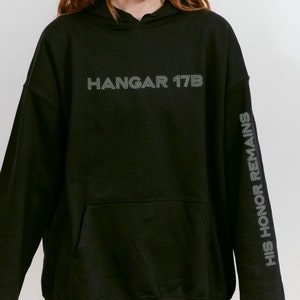 May include: Black hooded sweatshirt with the text "HANGAR 17B" on the front and "HIS HONOR REMAINS" on the sleeve.