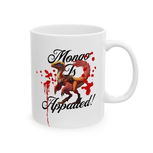 May include: White ceramic mug featuring a colorful dinosaur illustration with the text "Mongo Is Appauled!" in black script. The design includes red splatter accents, adding a dynamic visual element to the mug's design.