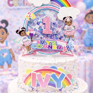 以下が含まれることがあります： 虹と「IVY」の名前が付いた、多層の誕生日ケーキ。ケーキは、数字「1」、雲、虹、そして「IVY'S CORNER ABC」の文字が特徴のトッパーで飾られています。ケーキには「あなたの誕生日の女の子を彼女自身のキャラクターに変えましょう」というテキストがあります。