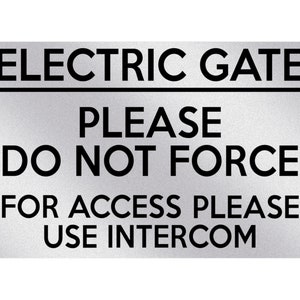 May include: A rectangular silver sign with black text. The sign reads "ELECTRIC GATE" above the line, followed by "PLEASE DO NOT FORCE" and "FOR ACCESS PLEASE USE INTERCOM".