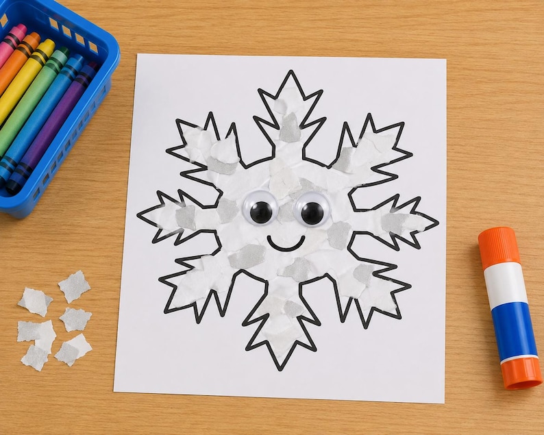 May include: A white paper cutout of a snowflake with black outlines, decorated with small white paper scraps, two plastic googly eyes, and a black drawn smile. A blue plastic basket with colorful crayons and a glue stick are nearby.